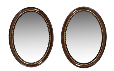 A pair of scumble framed, ebonised and parcel gilt slipped oval wall mirrors
