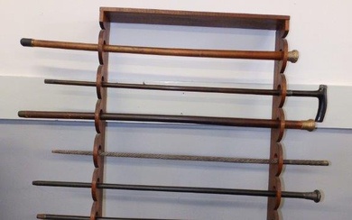 A wooden wall rack with three silver handled walking...