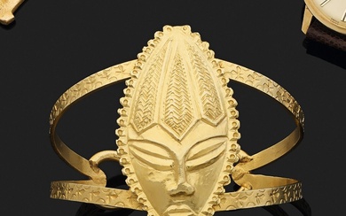 Bracelet rigide et ouvert en or jaune 750 millièmes, le centre décoré d'un masque anthropomorphe...