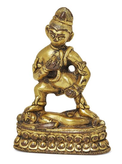 Property of a Gentleman (lots 36-85) A Tibetan gilt bronze figure of Kalajambhala, 16th century, cast standing in alidhasana trampling a prone figure, with right hand held to his chest clutching a kapala and the left arm restraining a mongoose, on...