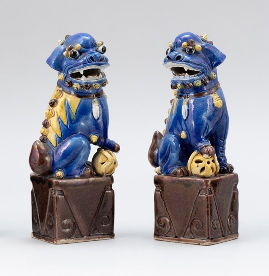 TWO CHINESE BLUE AND YELLOW GLAZED PORCELAIN FU DOGS Seated with brocade balls on aubergine bases. Heights 8.5".