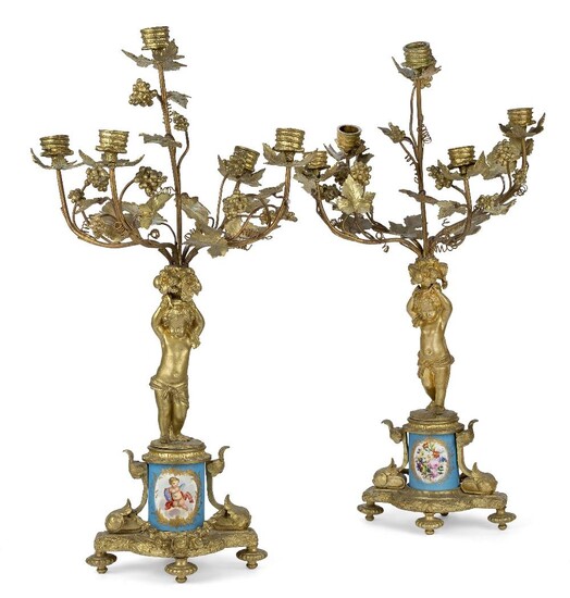 A pair of French Sevres style gilt-bronze and porcelain five light candelabra, 19th century, each with a central cherub holding aloft candle holders on foliate branches with leaf and berry decoration, on cylindrical Sevres style plinths with...