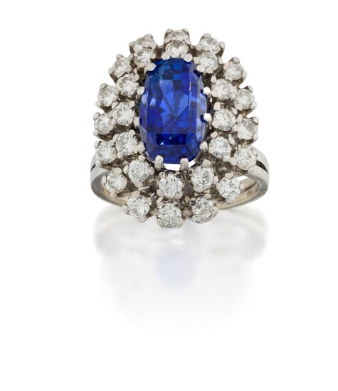 A sapphire and diamond cluster ring, the central modified step-cut sapphire weighing approximately 6.71 carats, in claw-set mount, within a double stepped row of brilliant-cut diamonds, to plain bifurcated hoop, approx. ring size L Accompanied by...
