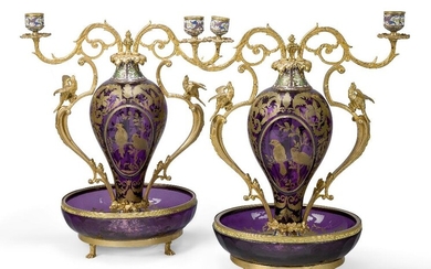 A pair of French gilt-bronze and champleve enamel mounted amethyst glass twin-light candelabra, 20th century, each with scroll branches above twin handles mounted with birds, the bodies gilt-heightened with foliage and reserves of birds, the dish...