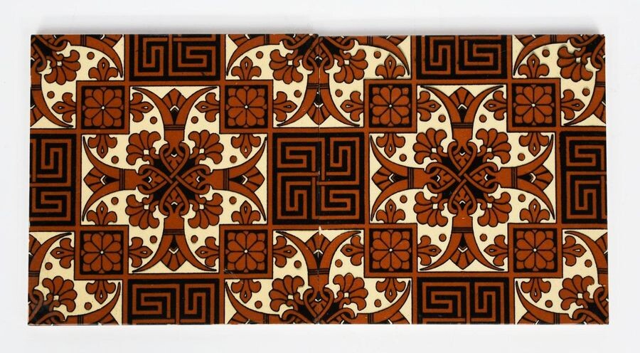 A pair of large Mintons China Works tiles designed by Dr Christopher Dresser, each printed in brown and black with a geometric flower, fleur de lys and Greek key repeat design, impressed marks, 20.5cm. square (2)