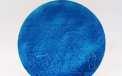 A Continental turquoise glazed plaque depicting a siege, early 20th century, the foreground with a commander of horseback and battery laying siege to a fortified town, 33.5cm diameter