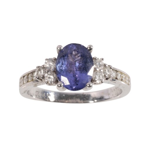 A TANZANITE AND DIAMOND RING the oval-cut tanzanite, flanked...