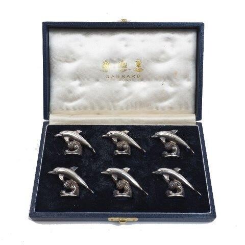 A cased set of six silver dolphin place card holders, by Garrard, London, 1997, each designed leaping over a breaking wave, 3.2cm high, in signed and fitted case, total weight approx. 9.9oz