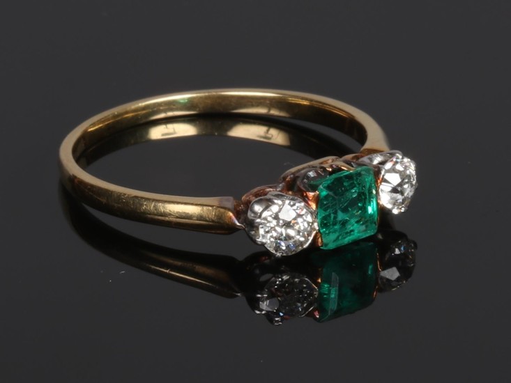 A yellow metal emerald and diamond three stone ring. With sq...