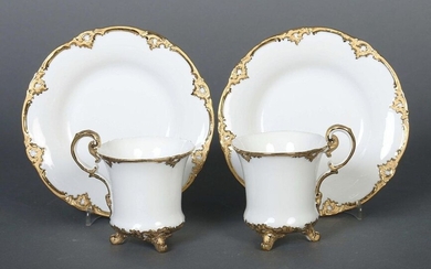 Two showpiece cups with lower Meissen, 1980ies, porcelain, glazed and decorated with a rich border of volutes and rocailles in matte and bright gold, the cup on three volute feet with curved handle, underglazed blue sword mark on the bottom as well as...