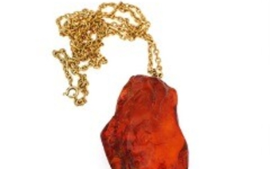 1927/1147 - A pendant of polished amber with eyelet of gold plated metal. L. 6.8 cm. incl. eyelet. Weight app. 20 g. Accompanied by necklace of gold plated metal.