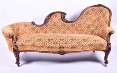 A large Victorian upholstered carved walnut chaise longue the frame carved with scrolls and floral motifs, upholstered with...