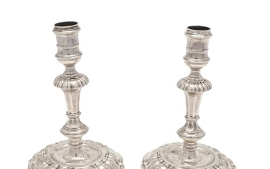 A PAIR OF GEORGE II CAST SILVER CANDLESTICKS. on shaped circ...