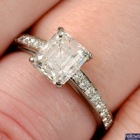 A platinum rectangular-shape diamond single-stone ring, with brilliant-cut diamond line shoulders.