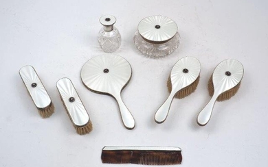 A white guilloche enamel and cut steel silver mounted vanity set, London, c.1960, maker TP, the set comprising: two hairbrushes (1965); two clothes brushes, (1964); a hand mirror (1965); a comb (damaged, 1965); a perfume bottle (1959) and a vanity...