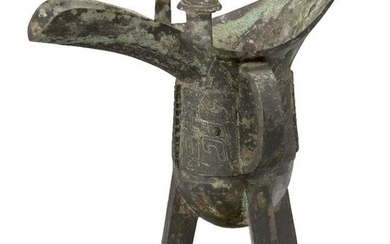 A Chinese bronze archaic wine pouring vessel, jue, late Shang dynasty, 12th-11th century BCE, finely cast with a band of two taotie masks on a leiwen ground seperated by notched flanges, beneath an upper band of blades rising towards the rim...