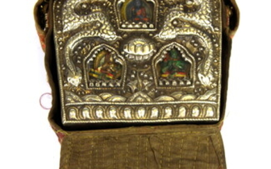 A large Tibetan hammered white metal and copper ga'u containing three painted clay Buddhist deities enclosed in a silk carrying case, L. 22c