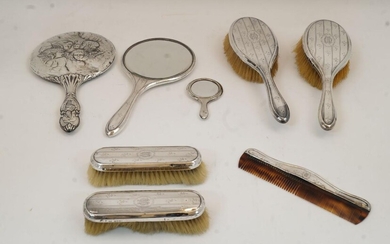 A six piece silver mounted vanity set, comprising: a hand mirror, four brushes, and a comb, Chester, 1919, James William Benson, with repeating floral motifs and central cartouche with monogram; together with a silver mounted hand mirror, decorated...