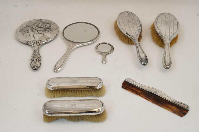 A six piece silver mounted vanity set, comprising: a hand mirror, four brushes, and a comb, Chester, 1919, James William Benson, with repeating floral motifs and central cartouche with monogram; together with a silver mounted hand mirror, decorated...