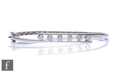 An 18ct hallmarked white gold hinged bangle, part channel se...
