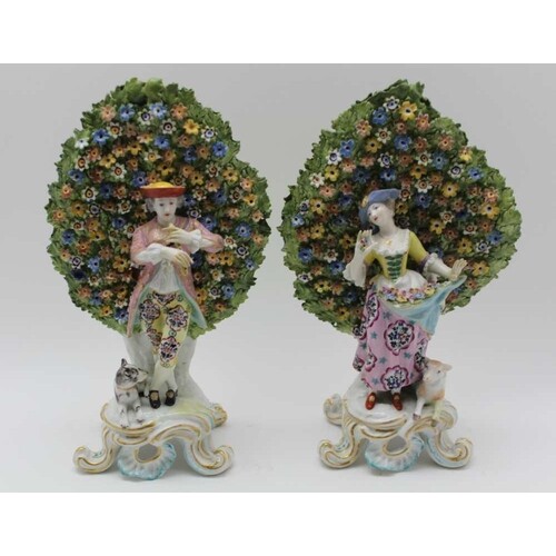 A PAIR OF PORCELAIN FIGURINES high floral bocage behind a pe...