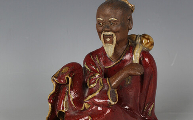 A Chinese sang-de-boeuf glazed stoneware figure of a seated sage, modelled with gourd water bottle s