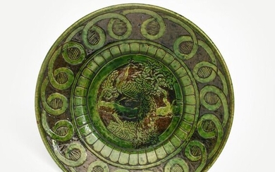 A Farnham Pottery charger, incised with a peacock perched in a tree bough, the rim with a band of loop decoration, in green on a brown ground, and two other Farnham Pottery vases unmarked, 36cm. diam. (3)