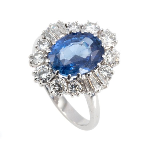 AN 18CT WHITE GOLD SAPPHIRE AND DIAMOND CLUSTER DRESS RING; featuring a blue oval sapphire estimated as 3.40ct to a border of 10 rou...