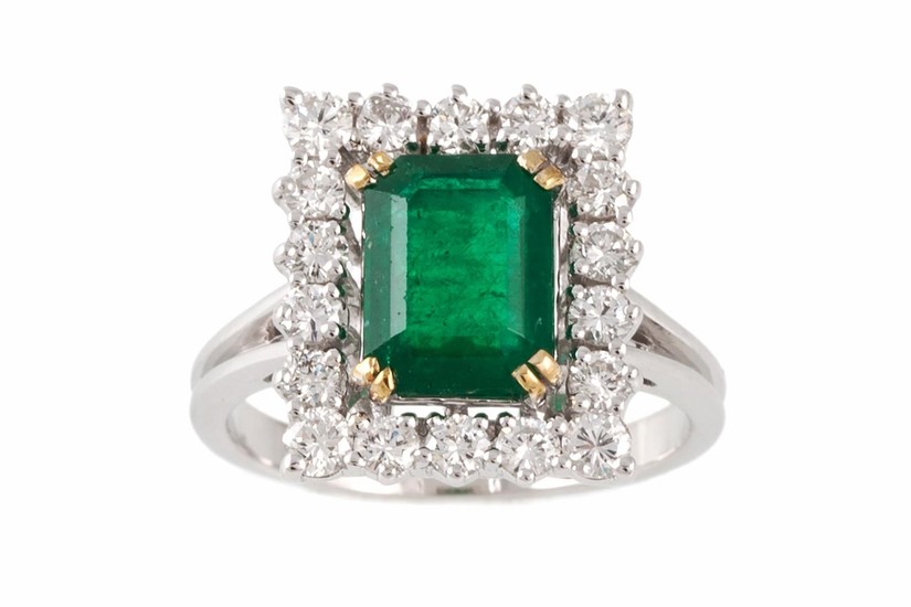 AN EMERALD AND DIAMOND CLUSTER RING, the trap cut emerald to...