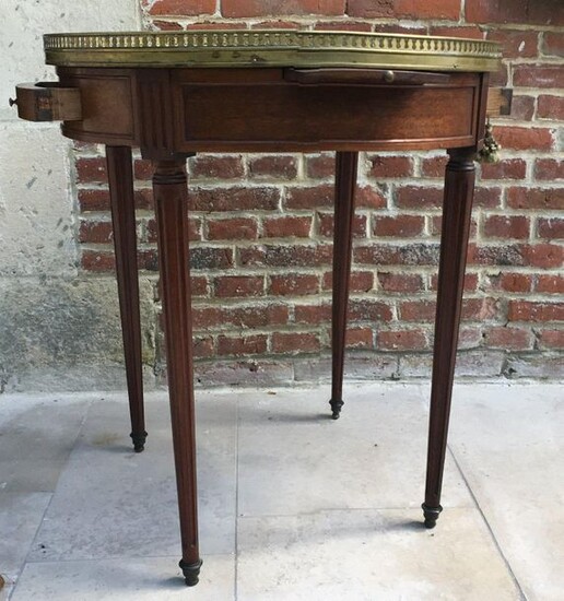 Mahogany and mahogany veneer bouillotte table resting on four ringed tapered legs. The white speckled marble top is underlined by an openwork brass gallery. It opens with a small pull-out forming a writing desk and a small drawer. Louis XVI style.
