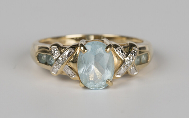 A 9ct gold ring, claw set with an oval cut blue topaz between diamond set 'X' shaped shoul