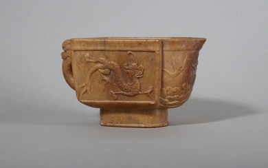 A CHINESE SOAPSTONE ARCHAISTIC 'DRAGON' POURING VESSEL. Ming Dynasty. The square-section body carved with dragons in low relief, the pointy spout with a flaming pearl above crushing waves, the back with a dragon head handle, all raised on a straight...