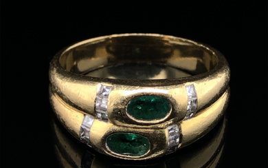 AN EMERALD AND DIAMOND RING. THE TWO OVAL CUT EMERALDS FLANKED WITH A CHANNEL SET OF PRINCESS CUT