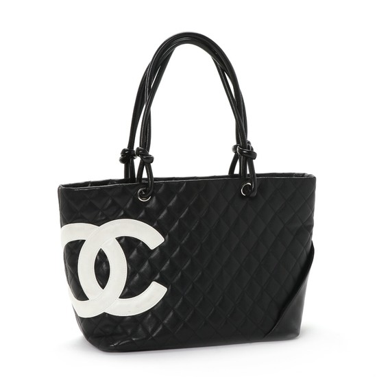 Chanel: A shoulder bag of quiltet black leather, white “CC” logo, leather handles, one large zipped compartment, a zipped inner pocket and an open inner pocket.