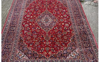 A hand knotted wool Kashan rug, rich red background with cen...