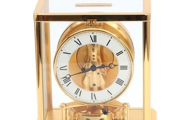 Jaeger-LeCoultre: “Atmos”. Brass and glass table clock, circular white enamel chapter ring. 20th century. H. 23. W. 20. D. 15 cm.