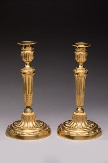 Pair of LOUIS XVI FLAMBEAUX in chased and gilt bronze. The shaft with rough grooves with asparagus tips, on a base with a laurel cord and a frieze of pearls. The vase style holders on pedestals with friezes of pearls. Original bobèches. Gilding with...