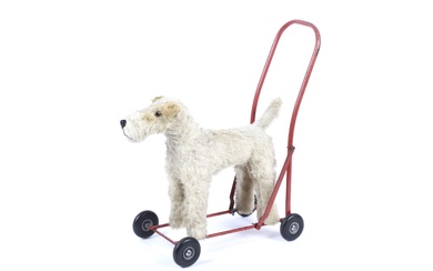 A mid-century Lines Brothers (Ireland) terrier push toy. In mohair, standing foursquare on a red painted metal frame with wheels, with label to underside of stomach, 47cm long inc. handle