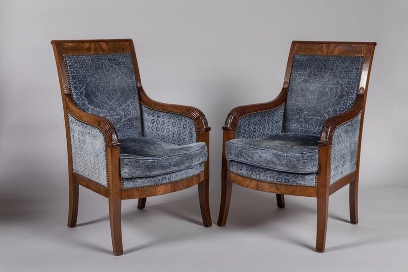 Pair of EMPIRE BERGERIES in mahogany and carved mahogany veneer, straight back, palm leaf armrests, scalloped ring and lotus leaves, curved belt. They rest on four saber feet. Empire-Restoration. Decorated with blue velvet with a bouquet of flowers in...