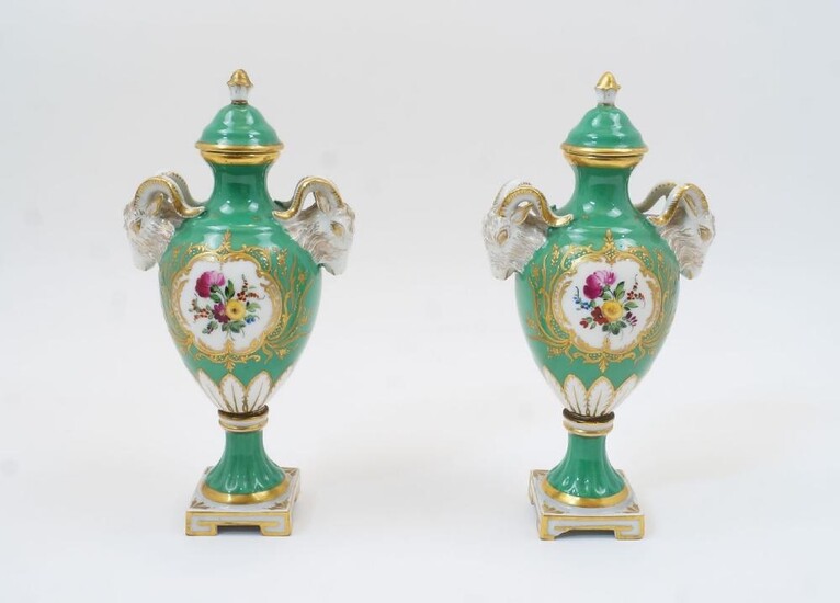 A pair of Dresden porcelain lidded urns with covers, late 19th century, blue marks to underside, of apple green ground with twin ram head lugs and cartouches containing floral sprays, on socle bases, 23cm high (2)