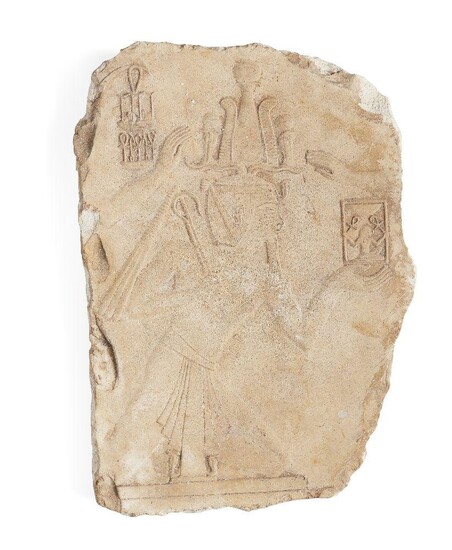 An Egyptian style limestone relief fragment of a kneeling pharaoh wearing a kilt, and an atef crown, holding a flail in his right hand while supporting a shrine with a kneeling figure within a rectangular naos, holding ankhs, the arm of a figure...