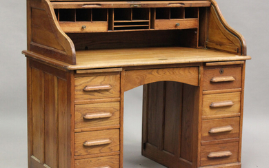 An early 20th century oak roll-top desk, the tambour shutter enclosing a fitted interior above an ar