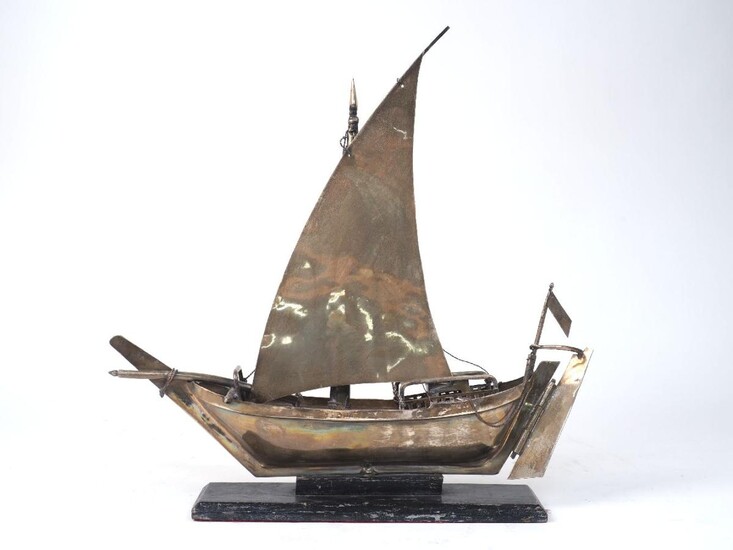 A white metal model of a boat with lateen sail, 20th century, mounted on an ebonised wood base, 40cm high overall