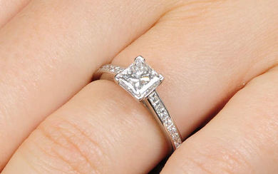 A platinum square-shape diamond single-stone ring, with calibre-cut diamond line shoulders.