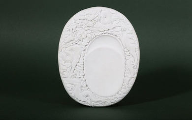 A CHINESE WHITE BISCUIT 'DRAGON' INKSTONE. Qing Dynasty, 19th Century, by Wang Binrong. The oval body moulded in high relief with two five-clawed scaly dragons contesting the sacred jewel amongst clouds, a four character Wang Binrong zuo seal mark to...