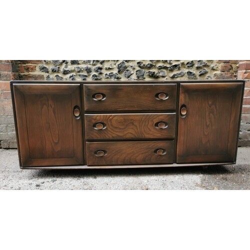A dark elm Ercol sideboard, with three central drawers, one ...