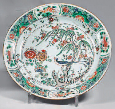 Small porcelain dish. Kangxi (1662-1722). Decorated with Green Family enamels, in the centre of a large tree with a bird and flowering rocks in a circled medallion, flowers thrown on the waterfall, the wing with fish and shrimps in interposed...
