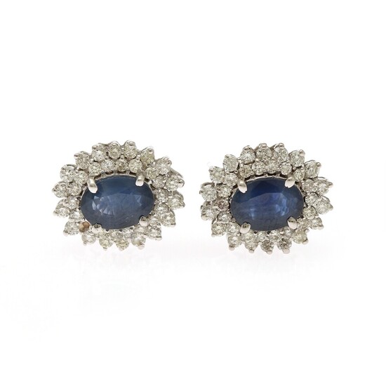 A pair of sapphire and diamond ear studs each set with an oval-cut sapphire encircled by numerous brilliant-cut diamonds, mounted in 14k white gold. (2)