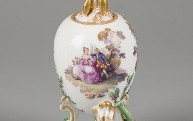A porcelain egg on legs and a leaf-shaped knob, decorated with classical scenes on both...