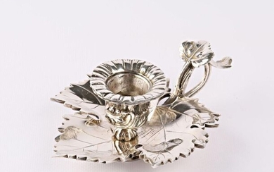 A silver bronze candleholder in the shape of a vine leaf supporting a small bowl finished in a corolla and hemmed with a frieze of foliage at its base, the socket showing a vine stock.